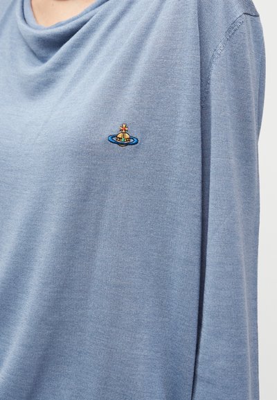 Ανοιχτό γαλάζιο πλεκτό τοπ με ντραπαρισμένο ντεκολτέ και μακριά μανίκια. Διαθέτει ένα μικρό κεντητό λογότυπο σε αντίθετα χρώματα στο αριστερό μέρος του στήθους.