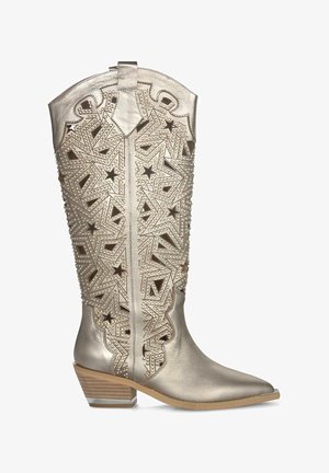 Metaliczne złote skórzane kowbojki z wyciętym wzorem gwiazdy, spiczastym noskiem i średnim blokowym obcasem. Posiadają dekoracyjne ćwieki i pętelkę u góry.