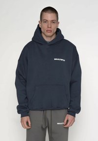 Felpa con cappuccio blu navy realizzata in tessuto morbido, con tasca frontale e logo bianco "MULTIPLY" sul petto. Design a vestibilità ampia, maniche lunghe.
