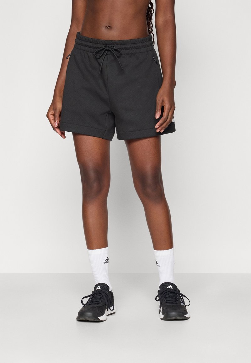 Černé sportovní šortky s elastickým pasem a šňůrkou. Nošené s bílými ponožkami Adidas a černými běžeckými botami. Hladká, lehká látka.