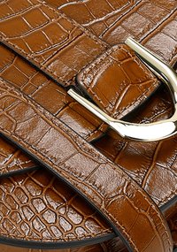 Bruine handtas van krokodillenleer met reliëf, voorzien van een glanzende zilveren gesp, met een gestructureerd oppervlak en contrasterende zwarte stiksels.