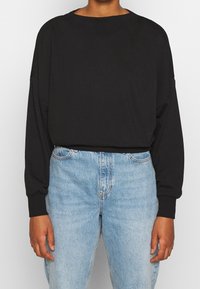 Sweat-shirt noir oversize en tissu doux avec manches longues. Associé à un jean bleu clair taille haute avec une texture denim classique.