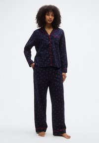 Ensemble de pyjama bleu marine avec passepoil rouge ; haut boutonné à manches longues et pantalon ample présentant un petit motif répétitif. Texture de tissu douce.