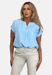 Jasnoniebieska bluzka z krótkim rękawem z dekoltem w kształcie litery V, wykonana z teksturowanej tkaniny. Posiada złote guziki akcentujące na rękawach. Połączona z kremowymi spodniami.