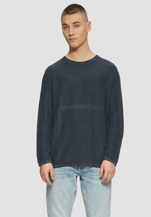 Marineblaue Langarmbluse aus einem weichen, strukturierten Stoff mit einem runden Ausschnitt und lässiger Passform, kombiniert mit hellblauen Jeans.