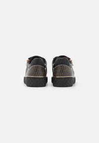 Black sneakers with textured finish and gold accents. Rear view shows embossed logo pattern and a solid black rubber sole with geometric grip.