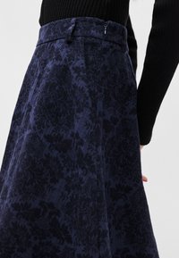 Σατέν φούστα με ναυτικό λουλούδι, κατασκευασμένη από υφή υφάσματος. Διαθέτει εφαρμοστό μέσο, πιέτες και κλείσιμο με φερμουάρ στο πλάι.