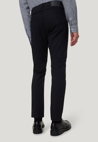 Schwarze Slim-Fit-Hosen mit Gesäßtaschen, flachem Frontdesign und Gürtelschlaufen. Kombiniert mit einem karierten Hemd und schwarzen Schuhen. Glatte, matte Stofftextur.