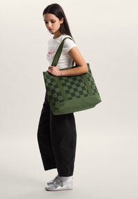 Zielona torba na ramię w kratkę, wykonana z trwałej tkaniny, wyposażona w solidne uchwyty i przestronny design.