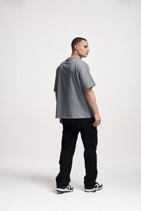 Tricou gri, cu mânecă scurtă și o croială lejeră, asociat cu pantaloni cargo negri, prevăzuți cu multiple buzunare și adidași albi.