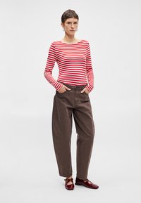 Červené a biele pruhované tričko s dlhým rukávom, hnedé široké nohavice a červené topánky. Tričko má lodičkový výstrih. Nohavice majú zapínanie na gombík.