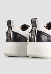 Sneaker bianche con toppe in pelle nera sul tallone, caratterizzate dal marchio "SMITH X" sui tiranti e spesse suole in gomma bianca.