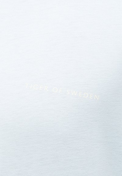 Ανοιχτό γκρι ύφασμα με διακριτικό κείμενο "TIGER OF SWEDEN" τυπωμένο στο κέντρο σε ελαφρώς πιο ανοιχτή απόχρωση.