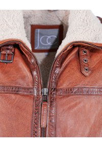 Bruine leren jas met een ritssluiting aan de voorkant, schapenwollen voering en drukknoopaccenten. Heeft een gestructureerde afwerking en detailwerk langs de naden.