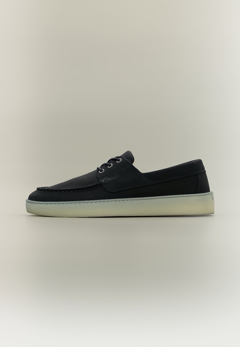 Μαύρο δερμάτινο casual παπούτσι τύπου boat με λευκή λαστιχένια σόλα και κορδόνια στο μπροστινό μέρος, εμφανίζεται σε ουδέτερο φόντο σε πλάγια όψη.