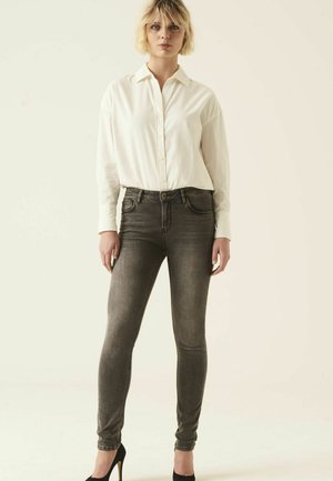 Jeans gris ajustados de cintura alta, con un diseño clásico de 5 bolsillos y un sutil desgastado. Llevados con una camisa blanca de botones y tacones negros.