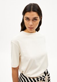 Crème kortebuik t-shirt van zacht katoen, met een ronde halslijn en een klein logo detail op de borst.