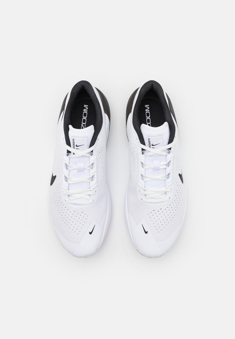 Zapatillas deportivas blancas con acentos negros, diseño perforado, cordones planos y suela texturizada. Presentan el logotipo de Nike en el costado y en la lengüeta.