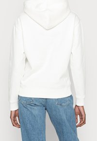 Sudadera blanca con capucha, de textura suave, con puños y cintura acanalados. Combinada con unos vaqueros de mezclilla azul claro, de corte relajado.