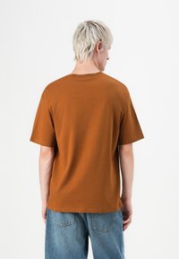 Brun bomulds T-shirt med korte ærmer, rund halsudskæring, løs pasform og en glat tekstur. Har en ensfarvet ryg uden synlige logoer eller detaljer.