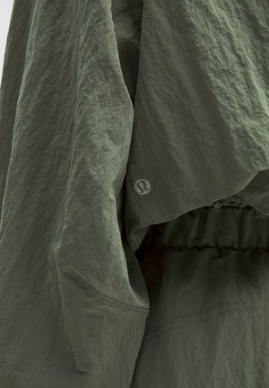 Groene lichte jas met een gestructureerde, gerimpelde stof. Heeft een elastische tailleband en een logo detail op de mouw.