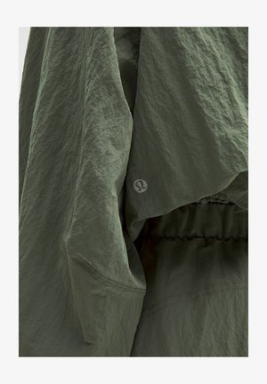 Groene lichte jas met een gestructureerde, gerimpelde stof. Heeft een elastische tailleband en een logo detail op de mouw.