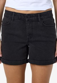 Juodų džinsinių šortų su apvyniotais kraštais, pasižyminčių prigludusia forma, priekinėmis kišenėmis ir sagų užsegimu juosmenyje.