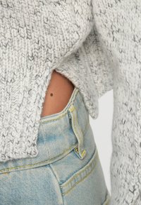 Maglione grigio chiaro a maglia con un motivo testurizzato, abbinato a jeans in denim blu sbiadito a vita alta con dettagli di cucitura gialla.