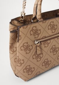 Ruskeakuvioinen käsilaukku, jossa on teksturoidusta kankaasta valmistettu pinta ja kultaiset metalliosat. Laukussa on vetoketjutasku ja kaksinkertaiset kahvat helppoa kantamista varten.