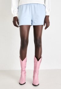 Lys blå bomullsshorts med elastisk midje, kombinert med rosa, blanke cowboyboots med spiss tupp og subtile designdetaljer.