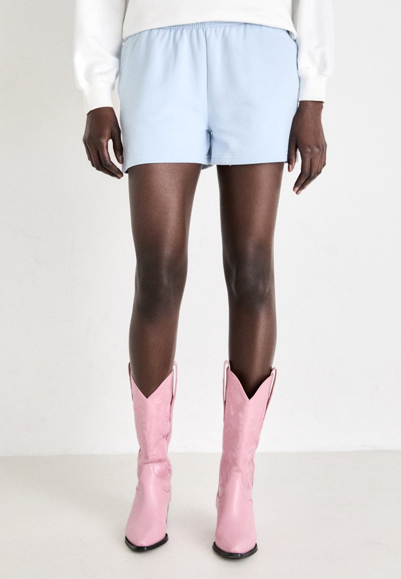 Lys blå bomullsshorts med elastisk midje, kombinert med rosa, blanke cowboyboots med spiss tupp og subtile designdetaljer.