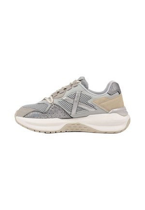Zapatilla deportiva en gris y beige con paneles de malla y textura, suela blanca gruesa y cierre de cordones, mostrada de lado sobre fondo blanco.