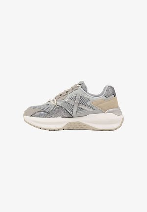 Zapatilla deportiva en gris y beige con paneles de malla y textura, suela blanca gruesa y cierre de cordones, mostrada de lado sobre fondo blanco.
