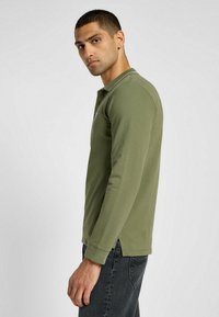 Långärmad polo skjorta i olivgrön, tillverkad av bomull, med krage, sidoflikar och en liten logotyp på bröstet.