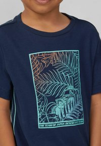 Navy-blaues Baumwoll-T-Shirt mit einem Grafikdruck von tropischem Laub und einem Fahrzeug, umrandet in Hellblau und Orange, mit Rundhalsausschnitt.