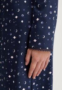 Abito in tessuto blu navy con motivi celesti bianchi e azzurri, inclusi pianeti e lune. Delicato bordo in pizzo sulle maniche.