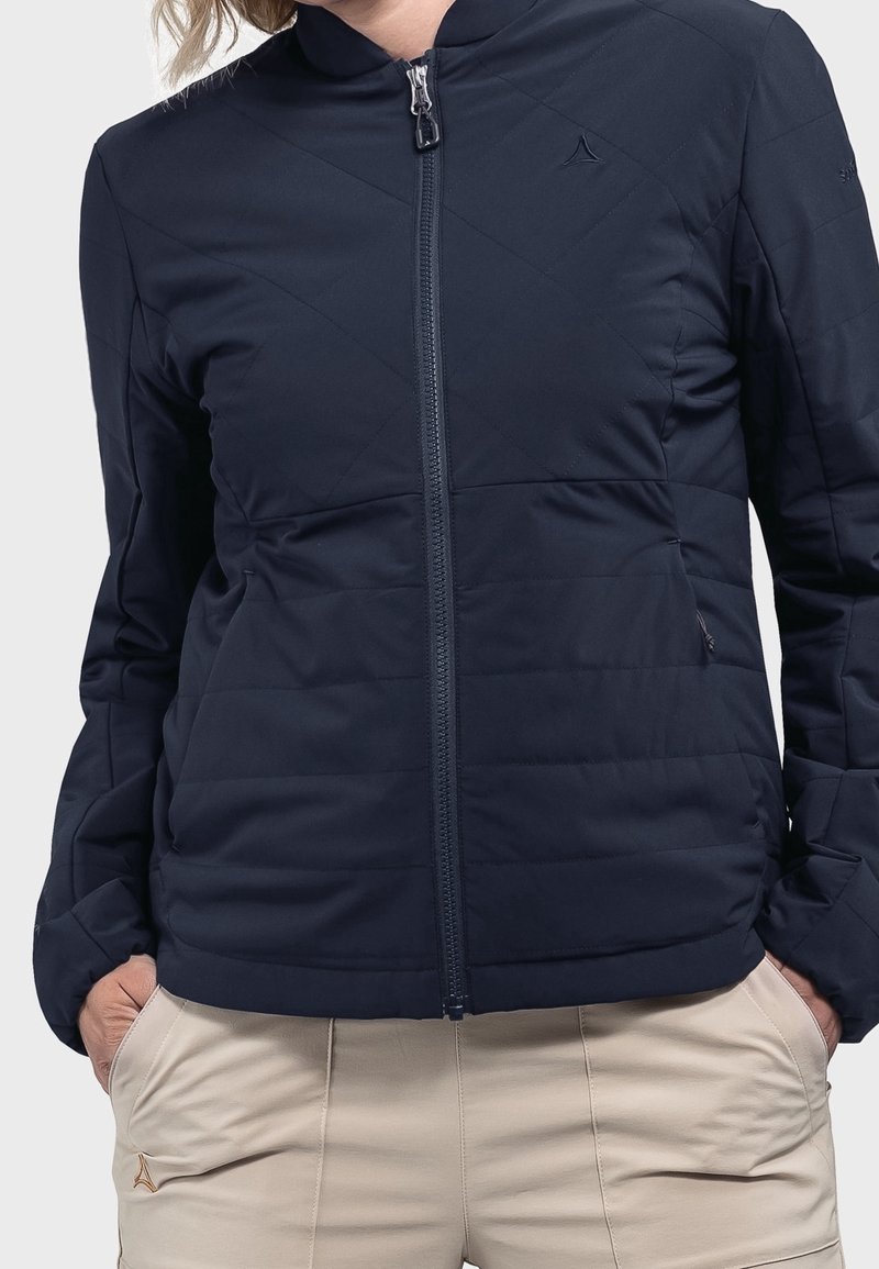 Granatowa pikowana kurtka z długimi rękawami, stójką i zamkiem błyskawicznym. Charakteryzuje się ukośnym przeszyciem i subtelnym logo na piersi.