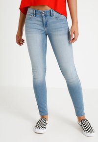 Ljusblå skinny jeans i denimtyg, med medelhög midja, subtil blekning och standard femfickdesign. Matchat med rutiga slip-on skor.