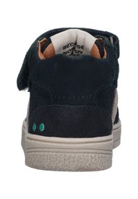 Marineblauwe suède sneaker met een beige zijpaneel, klittenbandsluiting en een lichtgekleurde zool. Beschikt over kleine turkooisaccenten op de hiel.