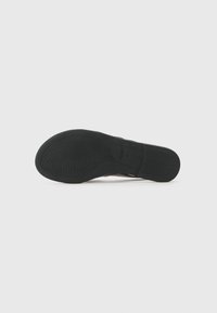 Schwarze Gummisohle mit strukturiertem Grip-Muster und geprägtem Logo-Detail, mit abgerundeter Form und glatten Kanten.
