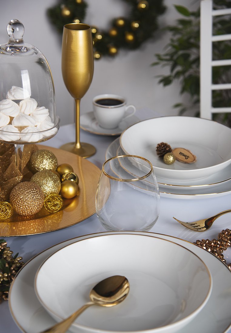 Weißes Geschirr mit goldenen Akzenten, Glasschüssel und goldenes Besteck auf einer hellen Tischdecke. Dekorative goldene und gläserne Ornamente sind präsentiert.