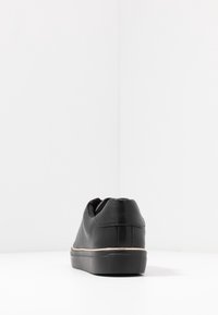 Svarta sneakers i texturerat läder, med en subtil tan-färgad accent längs sulan, rundad form och vadderad bakdel.