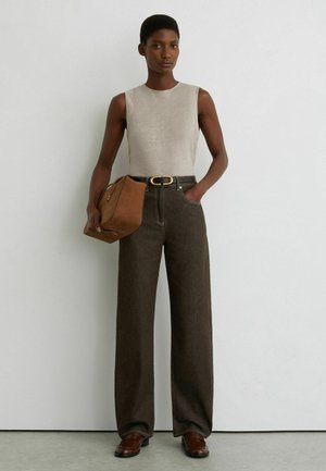 Kvinde iført ærmeløs beige top, højtaljede viddebukser i mørk farve, brun bælte, loafers og med en brun håndtaske.