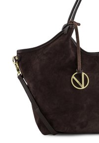 Brun ruskindshåndtaske med en glat tekstur, der har en cirkulær gulddetalje og læderrem. Dens form er blød og afrundet.