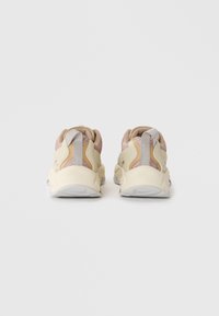 Sportliche Schuhe mit einem hellgelben und sandfarbenen Obermaterial, strukturierten Akzenten, einer gepolsterten Sohle und einer Lasche hinten für einfaches Anziehen.