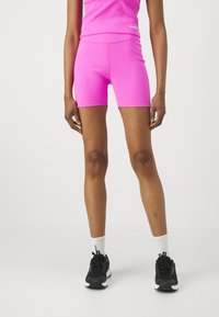 Rosa ribbede treningsshorts med en tettsittende design, kombinert med svarte joggesko og hvite ankelstrømper. Glatt tekstur, lengde over kneet.