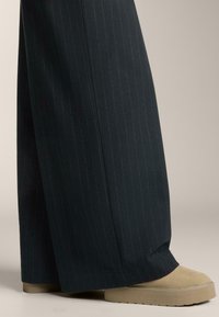 Hlače širokih hlačnic s črtami v temno mornarsko modri tkanini, kombinirane z bež platformnimi čevlji s gladko teksturo in rahlim peto.