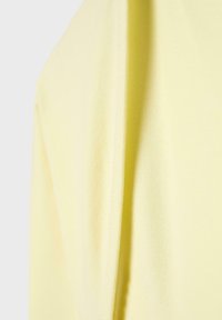 Približni posnetek mehke rumene tkanine z vidnim šivom, ki prikazuje teksturo in padec.