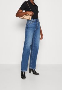 Jeans de corte recto en azul claro, hechos de denim. Combinados con una camiseta tipo polo negra y botas de tacón negro. Se lleva un bolso de mano color beige.