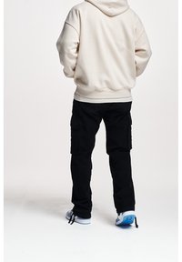 Beige mikina s volným střihem, kombinovaná s černými cargo kalhotami s bočními kapsami a světle modrými sportovními botami.